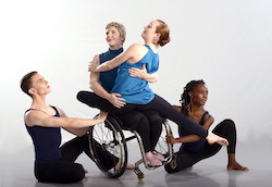 Laurel Lawson balances in a side tilt, holding a petite woman on her lap, both smiling. Two dancers wrap around them on the floor. Photo by Neil Dent, courtesy of Full Radius Dance.