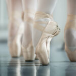 Dancers en pointe on a Marley dance floor.