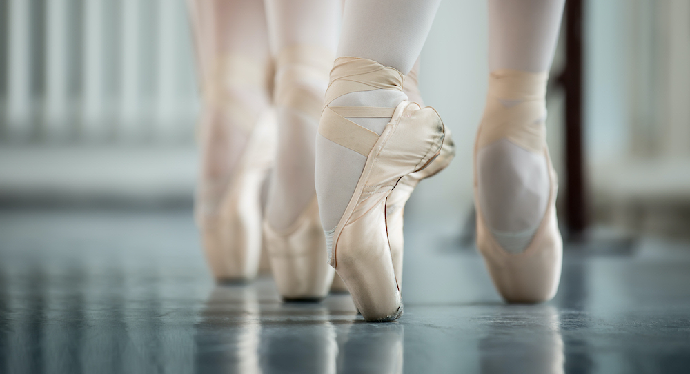 Dancers en pointe on a Marley dance floor.