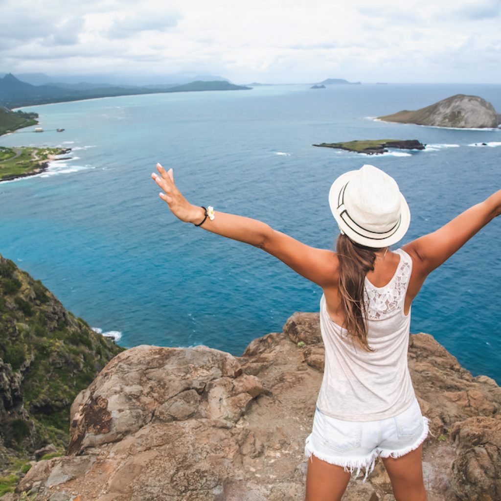 Woman traveler stands on top of a mountain with open arms and enjoys the fantastic landscape. Hiking people on Hawaii. Oahu island, USA.